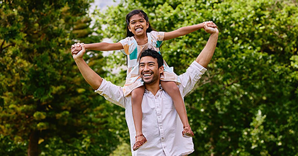 Daughter sitting on dad's shoulders in the park