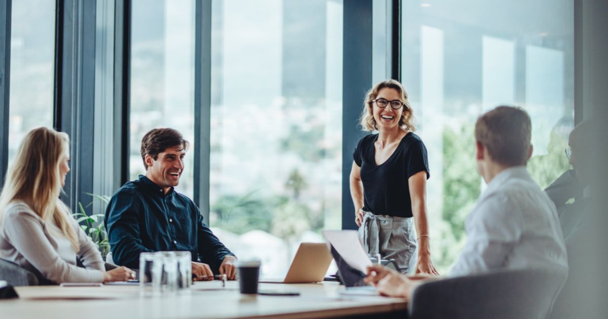 Woman smiling while standing in a boardroom meeting with peers.