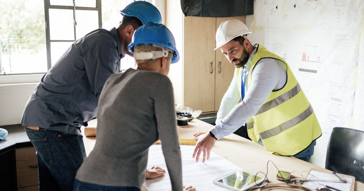 Two clients in hard hats meeting with general contractor discussing construction plans