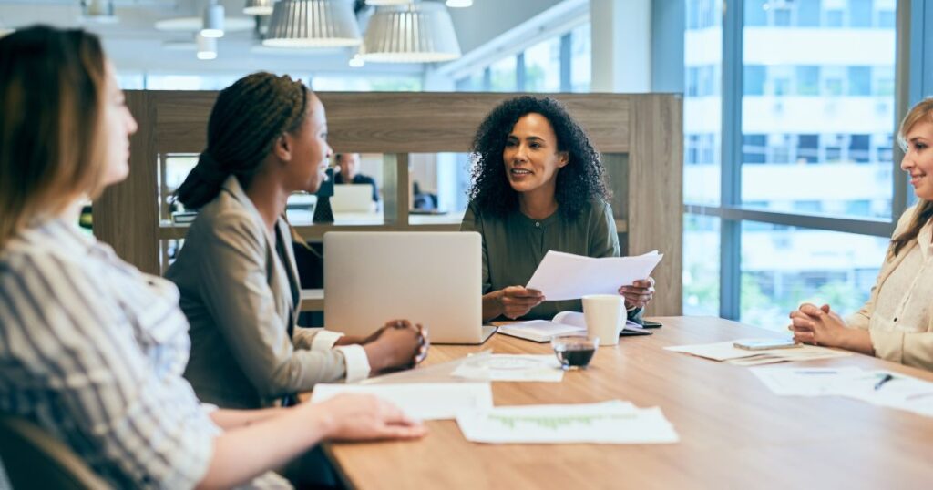 Four women meeting at a table reviewing papers