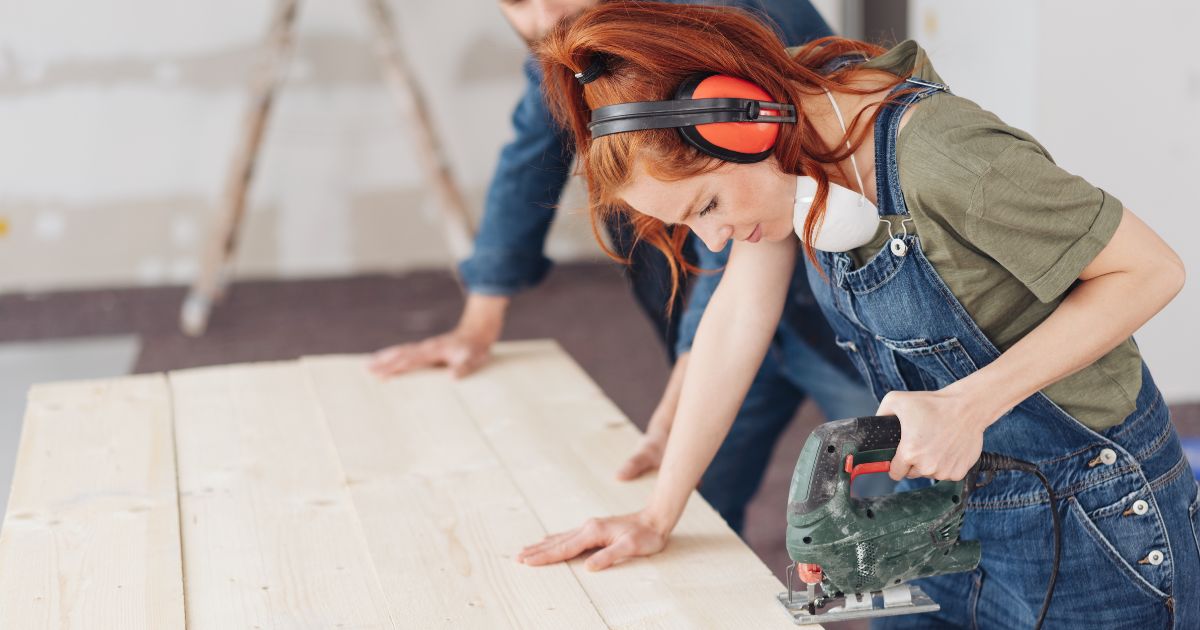 Woman with headphones using a hand saw to cut wood boards