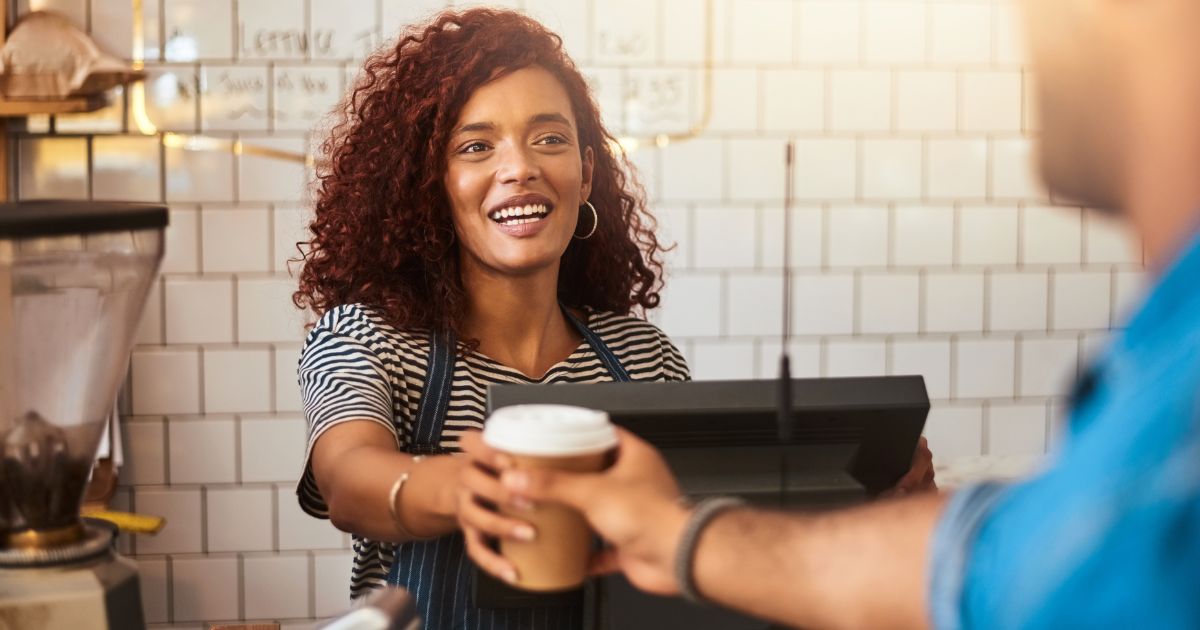 Woman behind cash register serving customer coffee