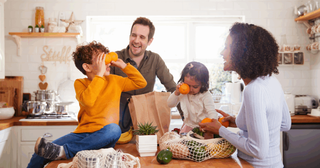 Family of four with two small children sitting on the kitchen counter unpacking groceries.