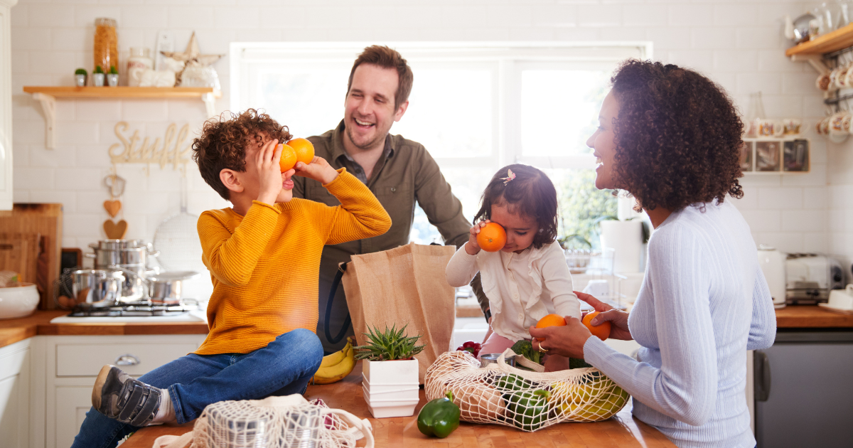 Family of four with two small children sitting on the kitchen counter unpacking groceries.