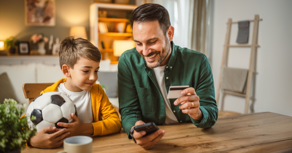 Father sitting at table with son holding a card and a phone