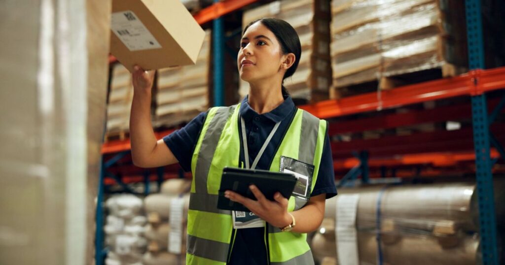 Woman working in warehouse holding tablet and moving boxes