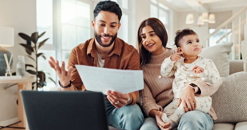 Young parents with baby sitting on couch reviewing papers