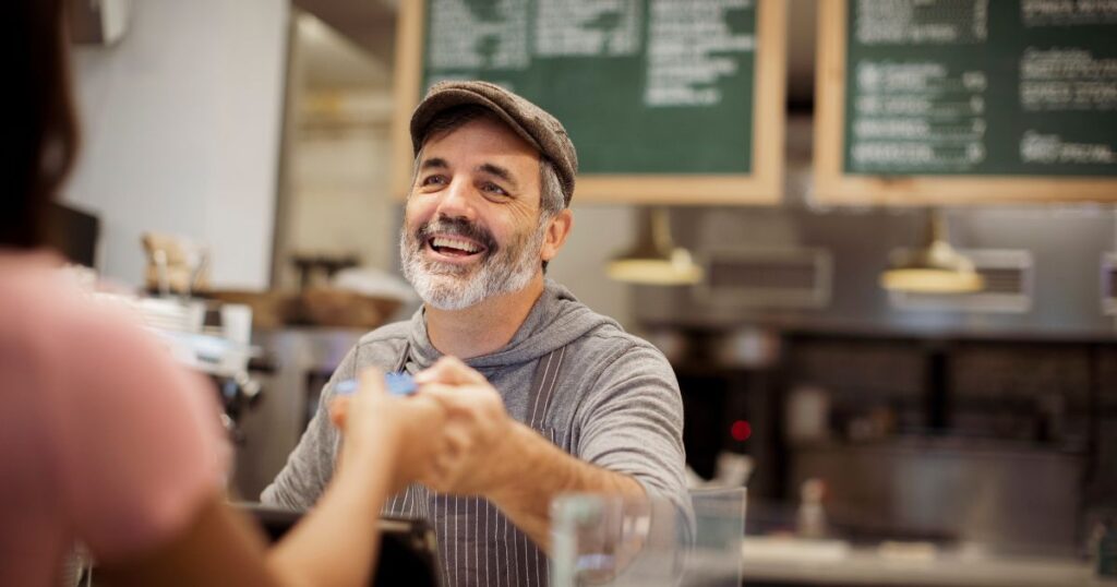 Man cashier in hat handing card to customer.