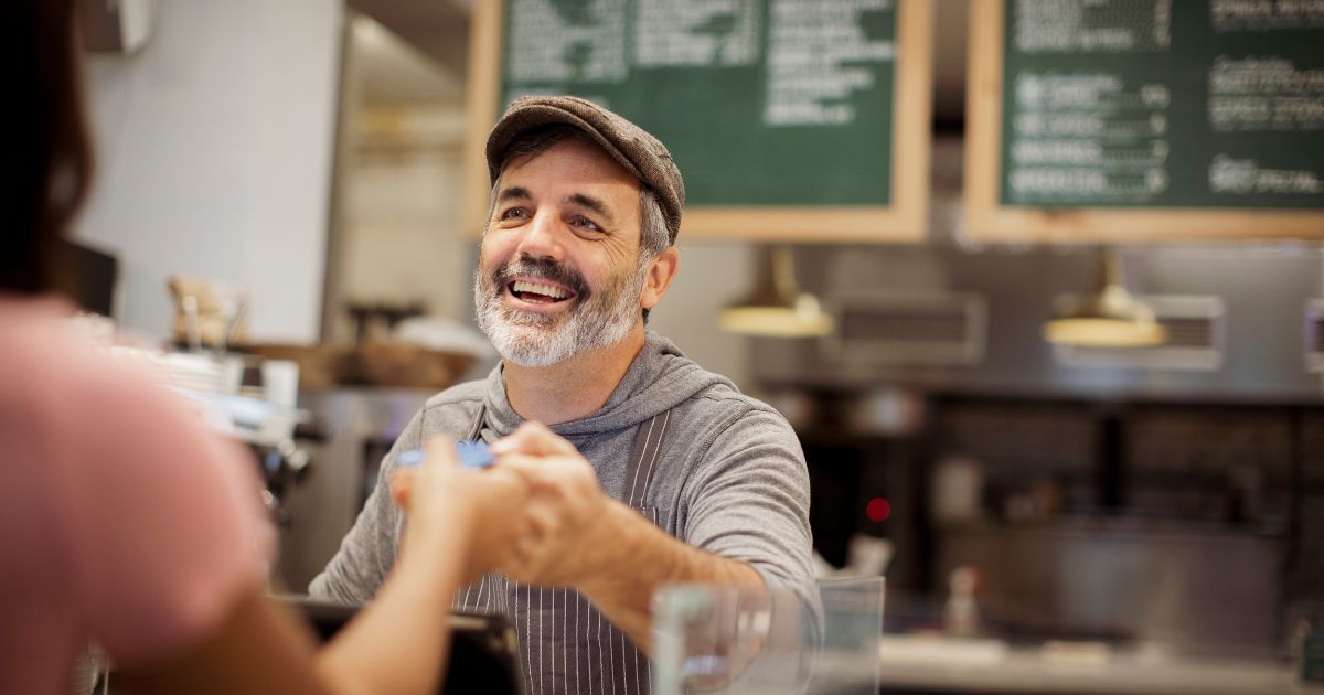 Man cashier in hat handing card to customer.