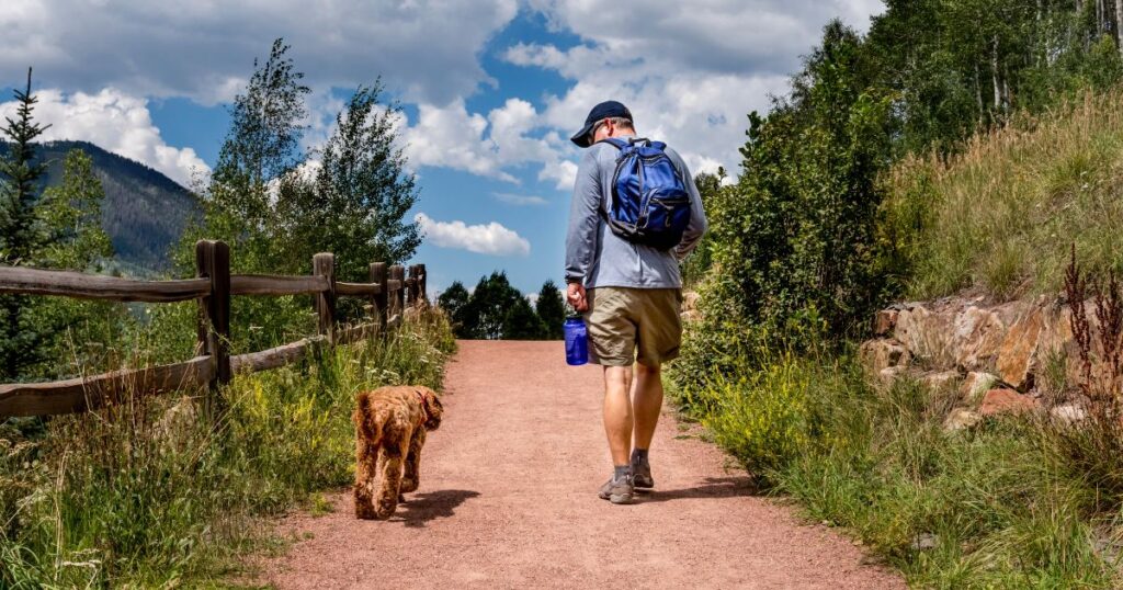 Man wearing a backpack on a scenic hike with his dog.
