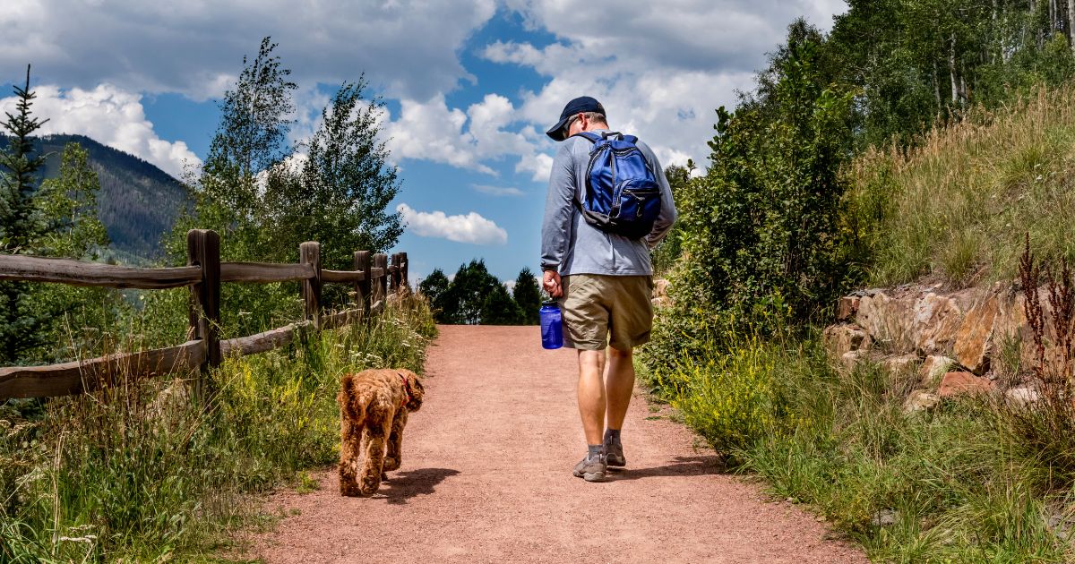 Man wearing a backpack on a scenic hike with his dog.