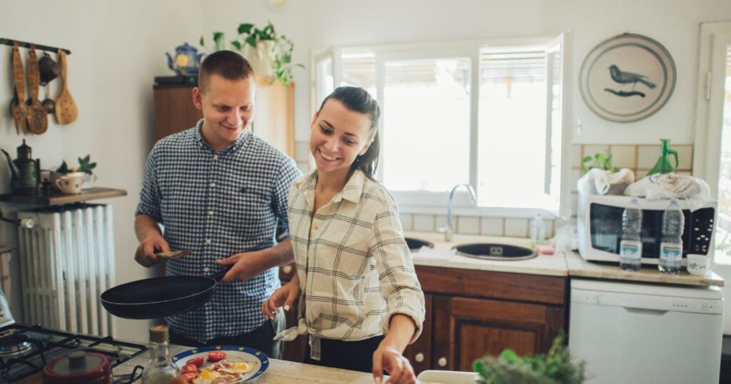 Young couple smiling while cooking food together over a stove.