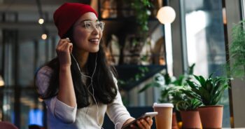 Young woman with headphones on smiling while sitting in a coffee shop.