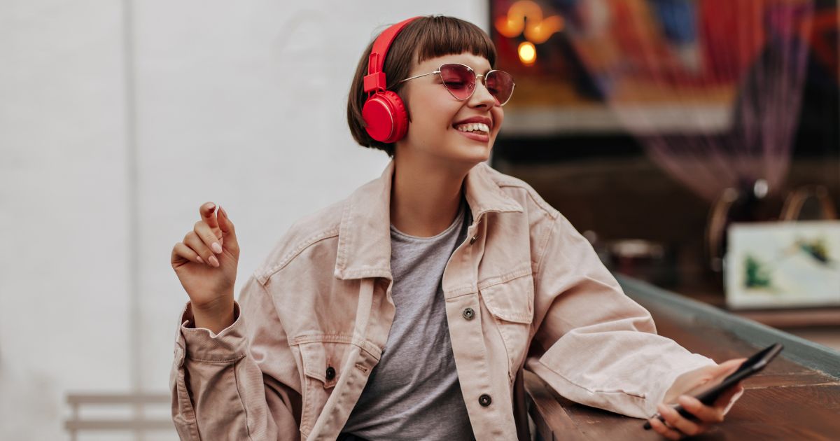 Young woman wearing red headphones sitting outside while holding her phone.