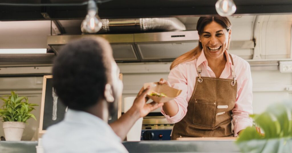 Woman smiling while serving a customer food from her food truck.