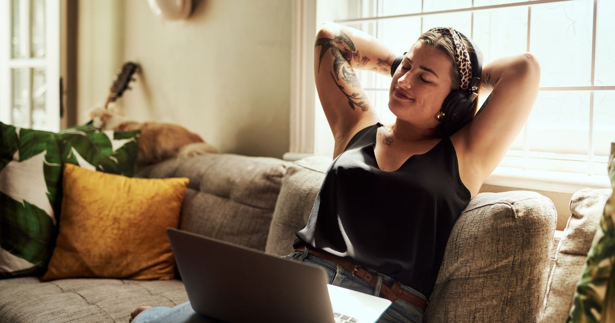 Young woman relaxing in her couch with a laptop and headphones on.
