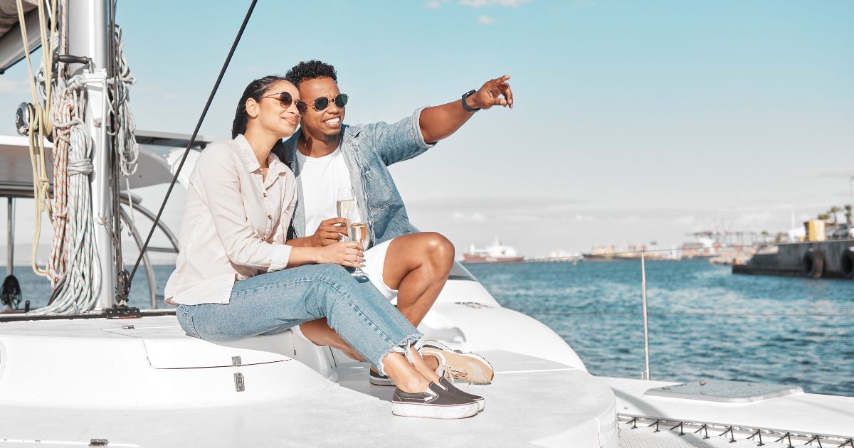 Young couple sailing on boat deck drinking champagne and pointing to the distance.